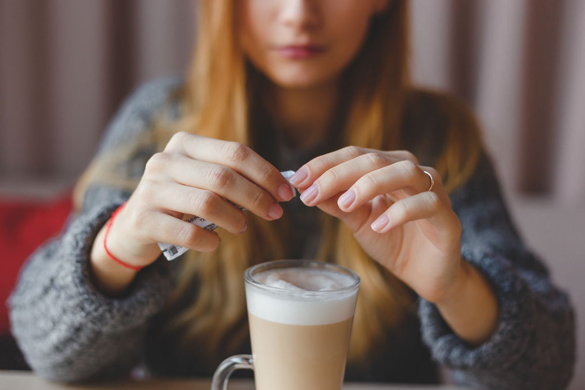 woman tearing open a sugar packet over a latte