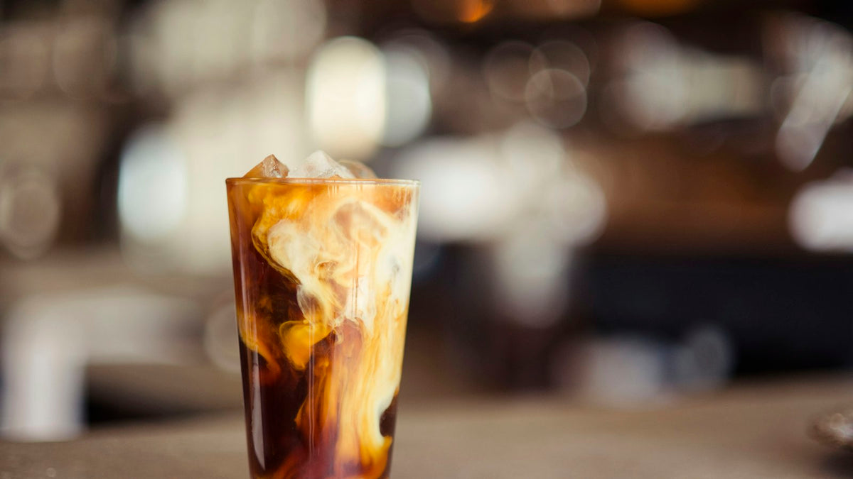 Iced protein coffee in a tall glass with milk swirling through the ice